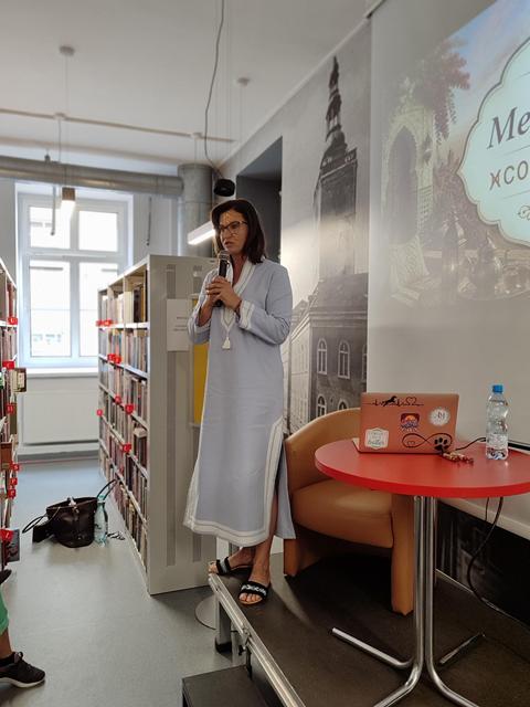 Prowadząca spotkanie Agnieszka Klech ubrana jest w tradycyjną marokańską tunikę. Występuje w bibliotece, w tle widać prezentację o Maroku.